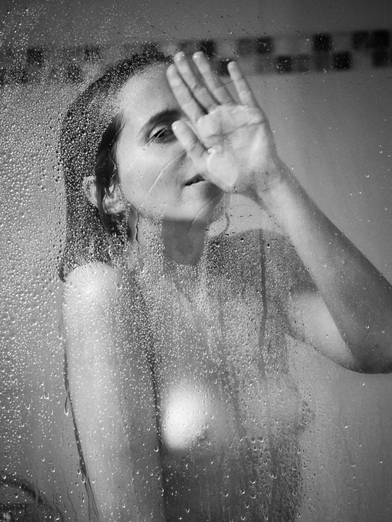 Portrait en noir et blanc d'une femme derrière une vitre couverte de gouttes d'eau photographiée par Antoine Cassane.