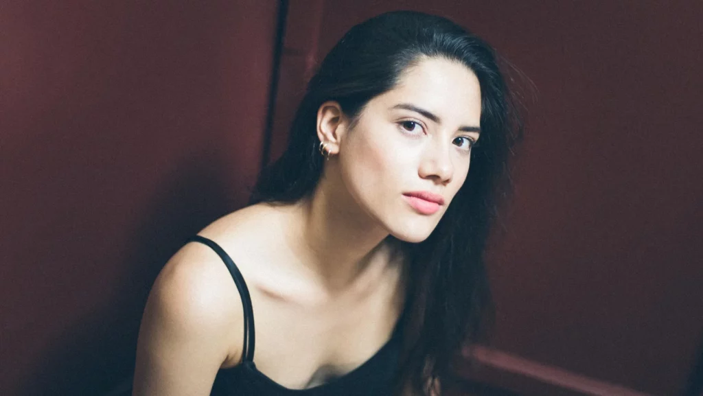 Portrait d'une femme regardant l'objectif devant un fond bordeaux, réalisé par le photographe Antoine Cassane.